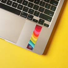 A picture of a laptop with a textured rainbow sticker on it by the mousepad.