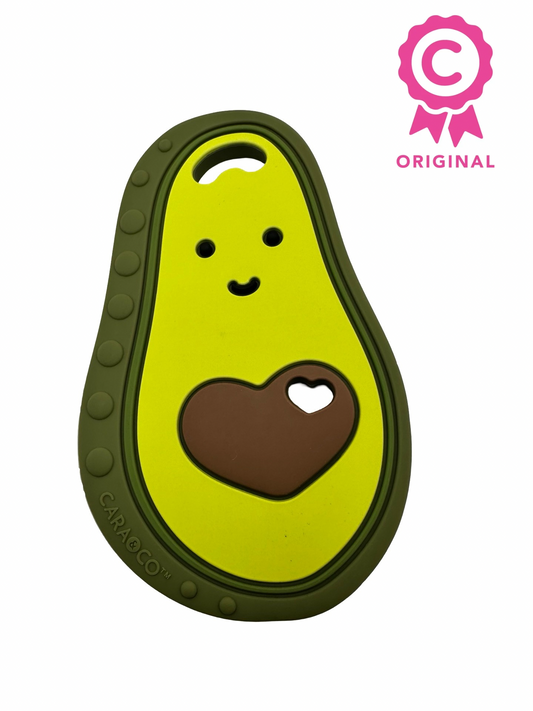 An avocado chewable teether. The pit is heart shaped, and there are eyes and a smile at the top. There is a badge in the upper right that says “C” with the word “original” underneath.