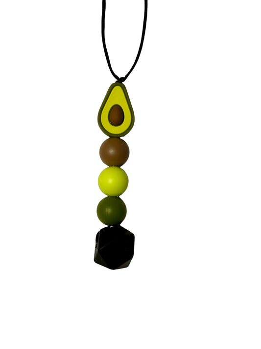 A bead chew necklace with an avocado at the top. There is then a brown round bead, light green round bead, dark green round bead and larger black hexagon bead.