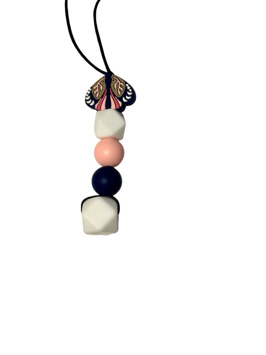 A navy moth is at the top of this bead chewable necklace. Followed by a white hexagon, a pink round bead, a navy round bead and a larger white hexagon.