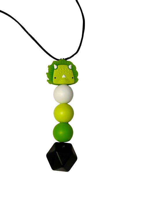 There is a triceratops dinosaur at the top. It is green. It is followed by three round beads in the following colours: white, light green and green. There is a black hexagon bead at the bottom.