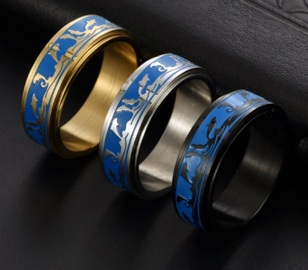 Three dolphin spinner rings in gold, silver, and black, each with a blue band featuring dolphin silhouettes.