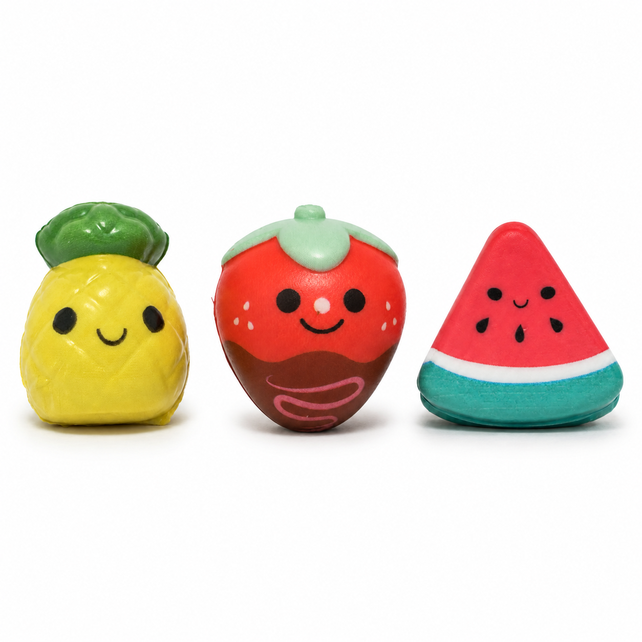 Three smiling fruit squishies displayed against a white background: a yellow pineapple, a chocolate-covered strawberry with pink drizzle, and a triangular watermelon slice.
