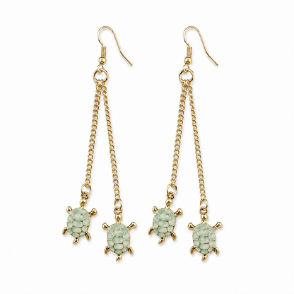 Pair of long gold-tone fish-hook earrings, each featuring two delicate chain drops finished with light green turtle charms, displayed against a white background.