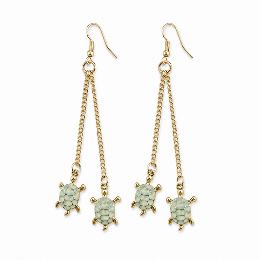 Pair of long gold-tone fish-hook earrings, each featuring two delicate chain drops finished with light green turtle charms, displayed against a white background.