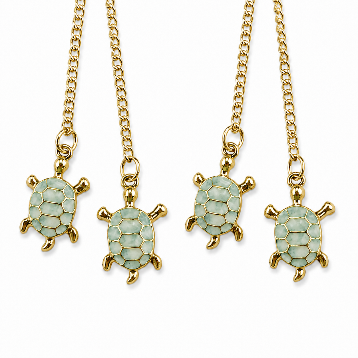 Close-up of four light green turtle charms with polished gold-tone outlines, hanging from fine gold-tone chains against a white background.