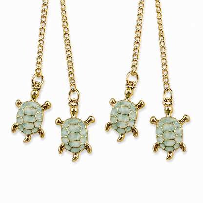 Close-up of four light green turtle charms with polished gold-tone outlines, hanging from fine gold-tone chains against a white background.